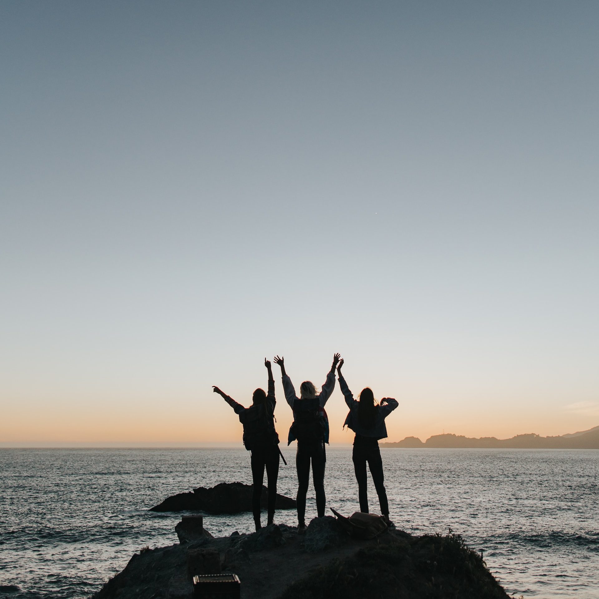 silhouette photography of persons raising hands while standing on island